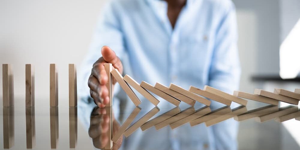 Person in light blue shirt stopping falling domino chain reaction with hand on reflective surface, symbolizing incident response plan.