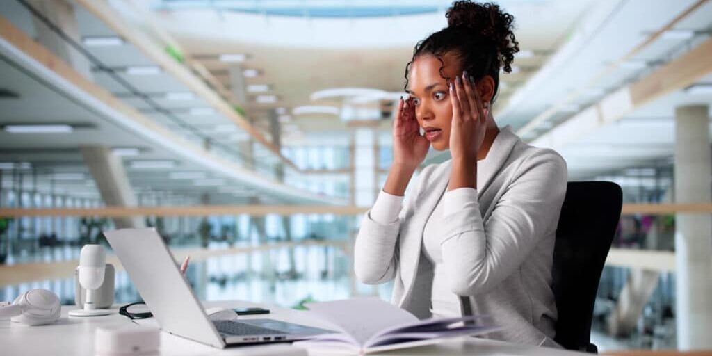 Stressed businesswoman at desk with laptop, reacting to potential data breach in modern office environment.