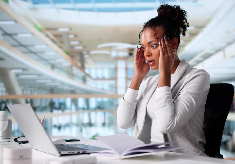 Stressed businesswoman at desk with laptop, reacting to potential data breach in modern office environment.
