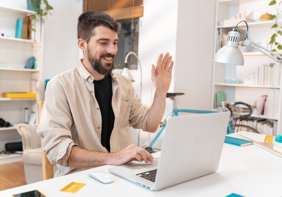 Young man smiling saying hello to work colleagues on computer desk